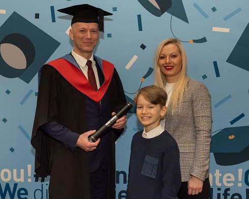Male wearing graduation robe pictured with wife and son