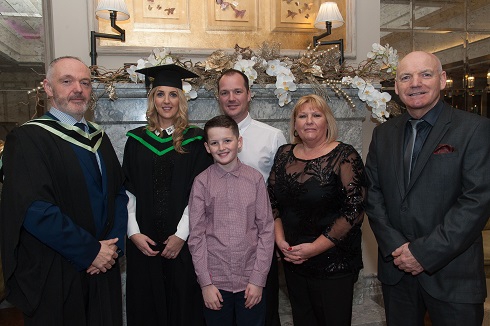 Female graduate in her gown pictured with her family in front of a fireplace in Galgorm Resort & Spa