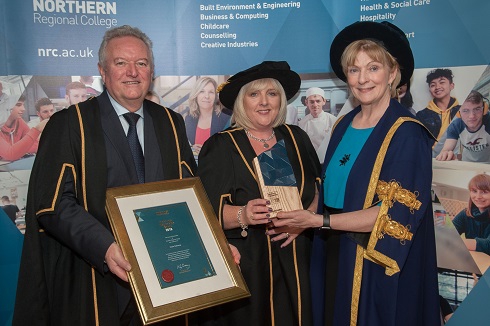 Female honorary fellow being presented with framed certificate by male and female Principal outside Galgorm Resort and Spa