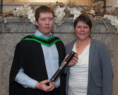 Male graduate with gown and scroll pictured with his mum
