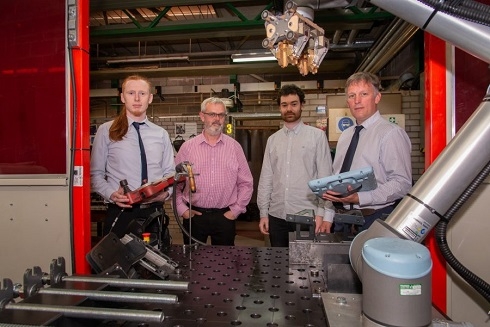 Four males standing around a robotic welding machine