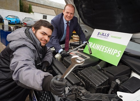 Two males standing under the bonnet of a car with a Traineeship sign