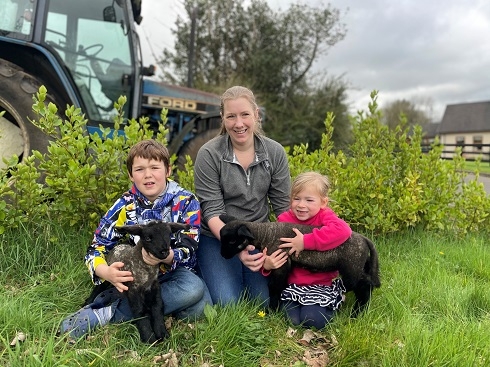 Female sitting with children holding lambs in a farm