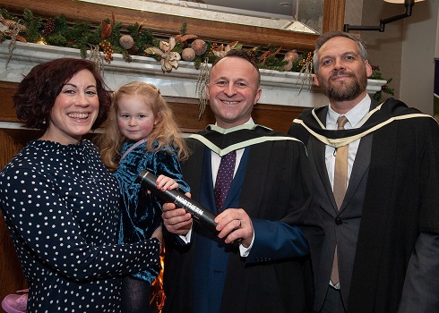 Male student in graduation gown with lecturer and his family