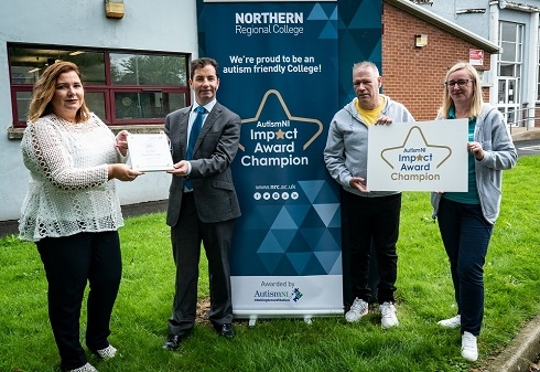 Male and Females holding an award and Autism NI impact award prop outside College building