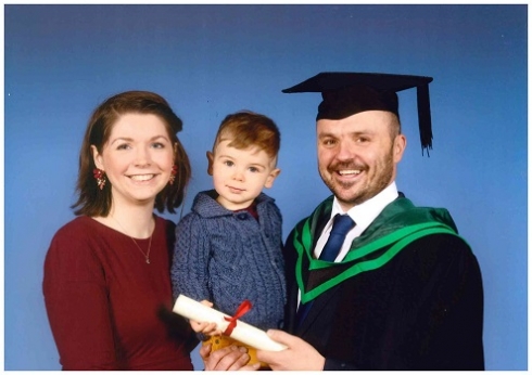 Male student in graduation robe pictured with family