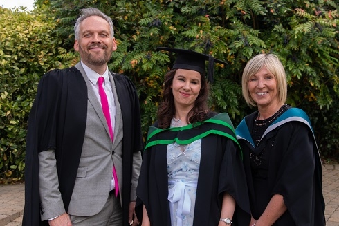 Female student standing alongside her lecturers in graduation gowns