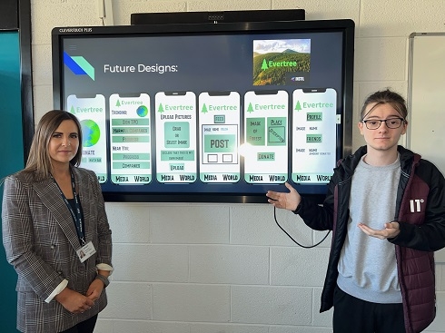 Female lecturer and male student standing next to plasma screen