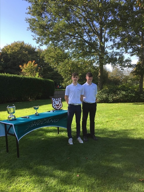 Tow males standing in garden next to trophies