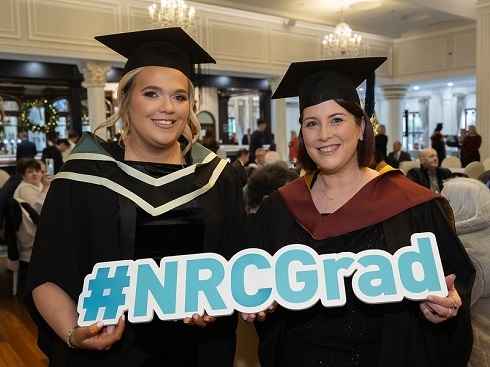 Two females in graduation gowns holding props