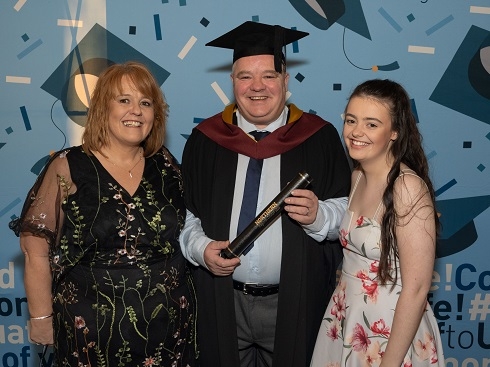 Male with graduation robe with wife and daughter