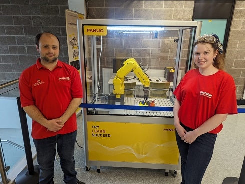 Male and female standing next to industrial robot