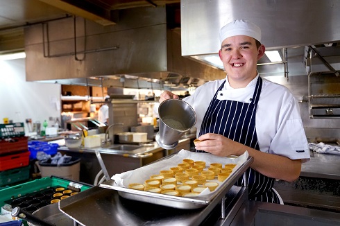 Female apprentice in kitchen in chef whites holding a tray of food