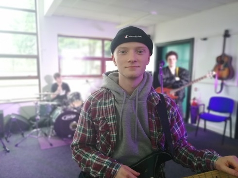 Male holding a guitar with band members in background
