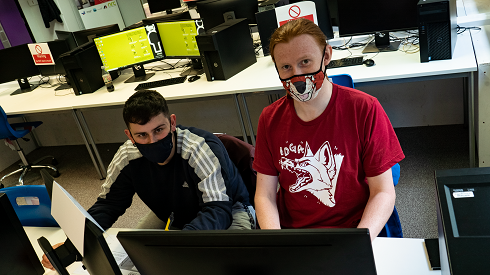 Two Males with Masks sitting at computer