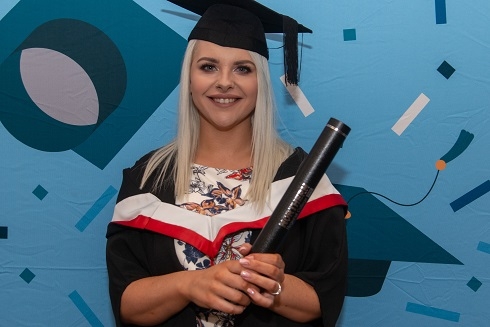 Female in graduation gown holding a certificate tube