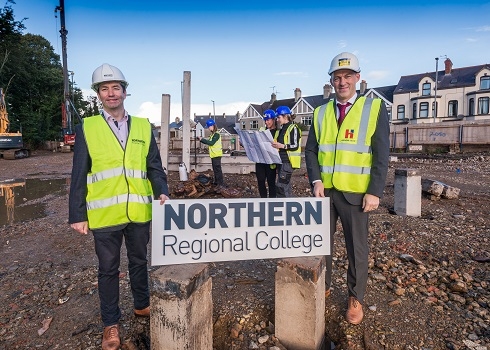 Two men with hard hats and high vis vests holding onto NRC logo prop