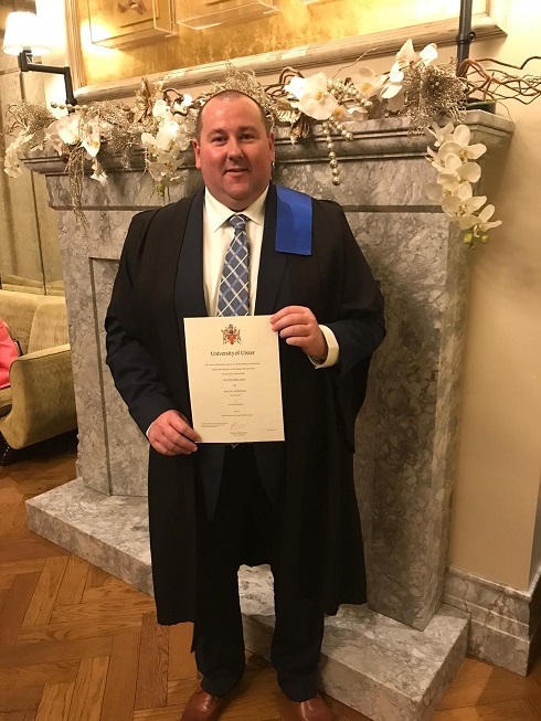 Male in gown holding a certificate