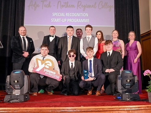 Group of students sitting on stage holding a Young Enterprise prop
