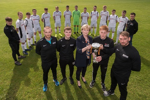 Football team pictured with Principal and coaches holding the cup