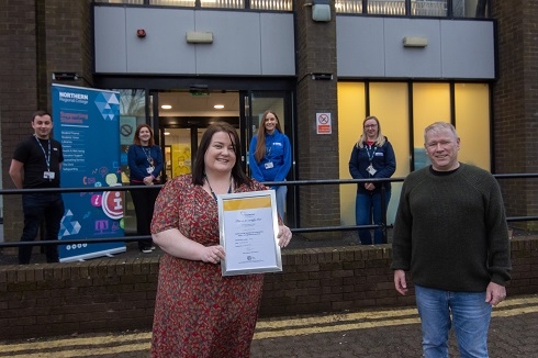 Staff standing out building, one holding a certificate