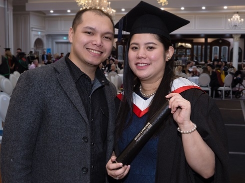 Female in graduation gown holding certificate tube with husband