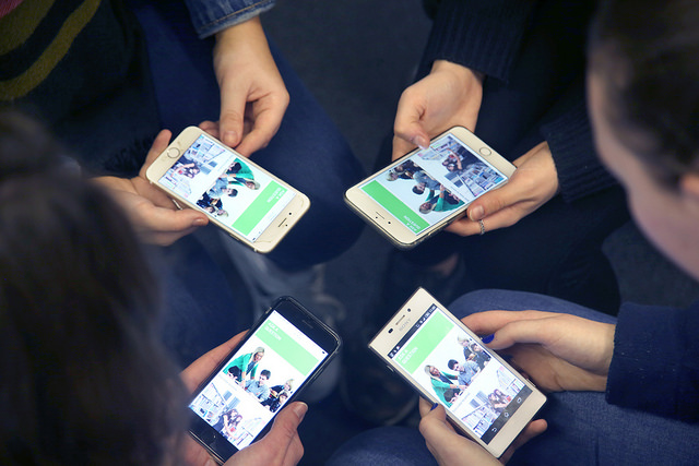 Four students holding mobile devices browsing College website.